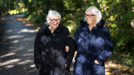 To ældre kvinder går arm i arm og griner sammen