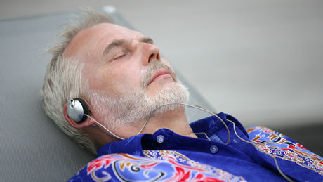 Mand, der ligger med lukkede øjne og høretelefoner på og lytter til musik